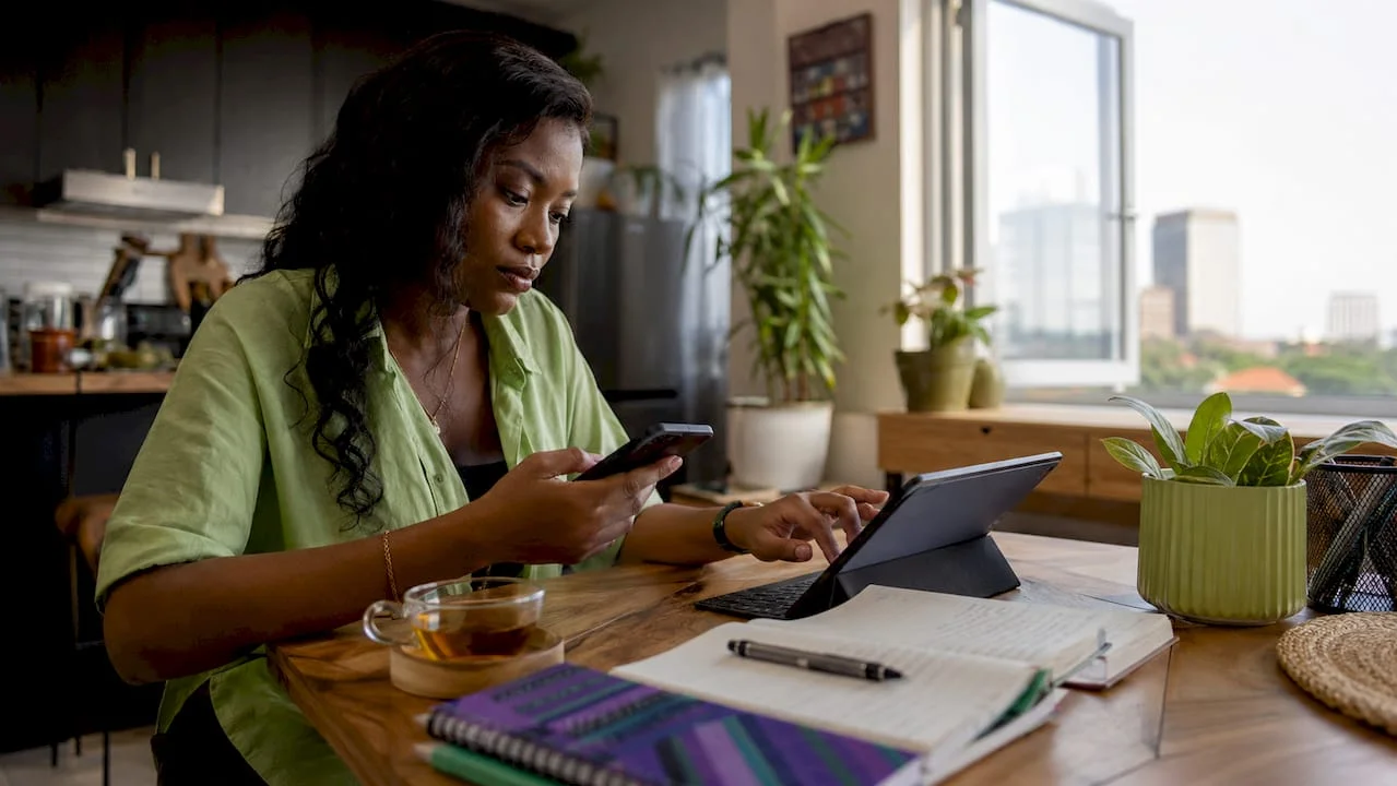 Nigerian woman verifying news on smartphone and laptop